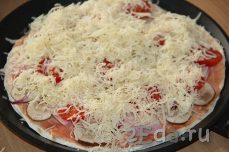 Поверх пиццы разложить кружочки помидоров, посыпать оставшимся натёртым сыром.