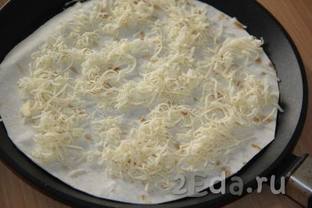 Сыр натереть на тёрке. Выложить один лист лаваша в сковороду (перед выкладыванием лаваша сковороду, при желании, можно немного смазать маслом), посыпать половиной натёртого сыра.
