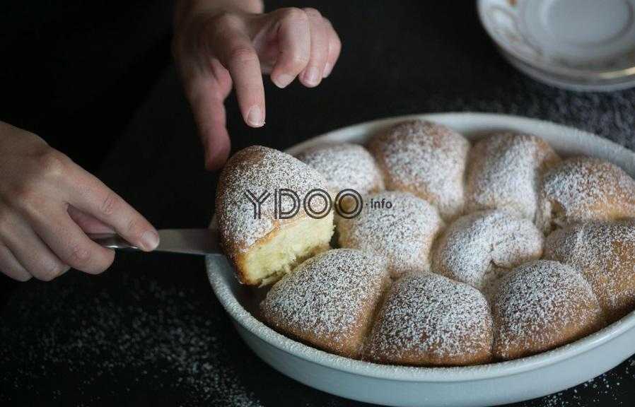 пышные булочки присыпанные сахарной пудрой, в форме для запекания, одну булочку достают лопаткой из формы