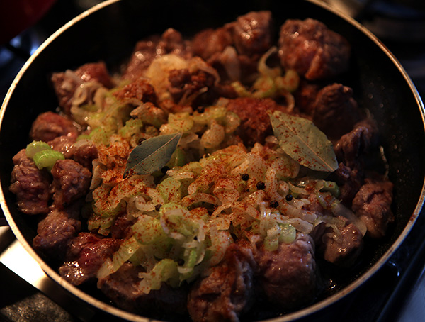 Добавляем к мясу лук и сельдерей, всыпаем паприку, лавровый лист и перец горошком, перемешиваем.