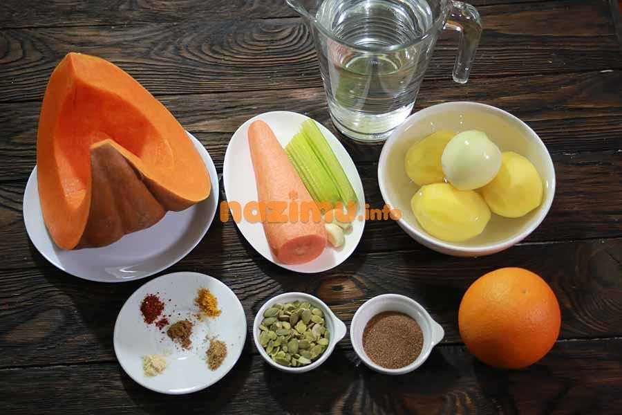тарелочки с тыквой, морковью, сельдереем, картофелем, репчатым луком, специями и тыквенными семечками, рядом графин с водой и свежий апельсин на столе