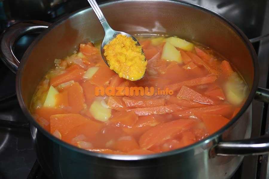 кипящий бульон с овощами в кастрюле, над ним ложка с тертой апельсиновой цедрой