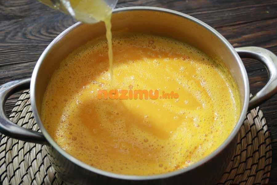 кастрюля с супом-пюре из тыквы, над ней стакан с апельсиновым соком, который добавляют в блюдо