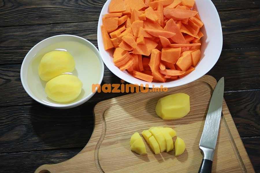 деревянная разделочная доска, на ней нож и нарезанная брусочками картошка, рядом тарелка с измельченной морковью и сырой картошкой в воде