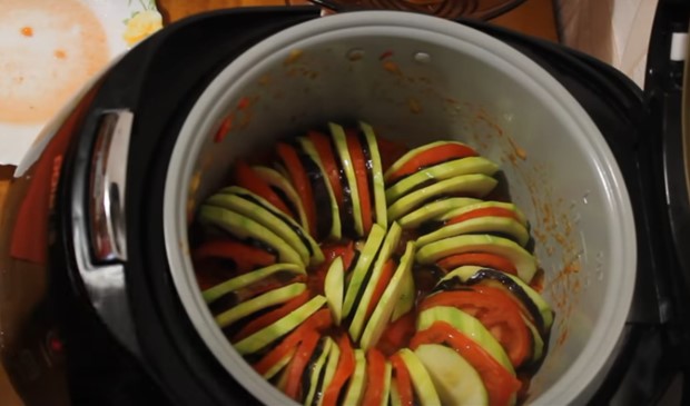 Отложить половину соуса в тарелку, а на оставшийся выложить овощные слайсы, чередуя между собой кабачок, помидор и баклажан.